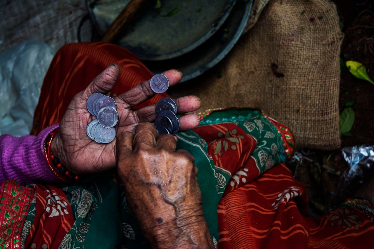heros-img Close-up of an elderly woman's hands counting coins on a colorful textile background.
