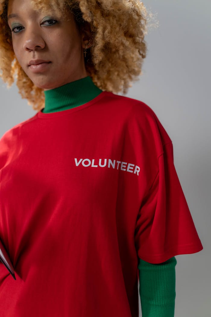 Confident young woman wearing a red volunteer t-shirt and green turtleneck, showcasing empowerment.