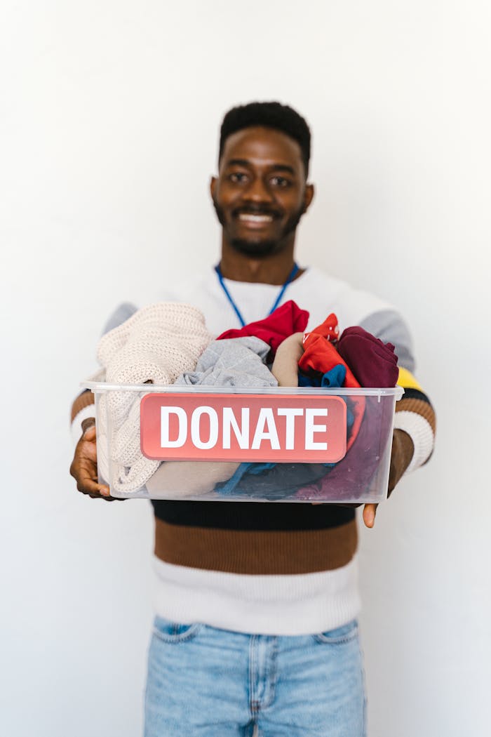 A cheerful volunteer holds a donation box filled with clothes, encouraging charitable giving.